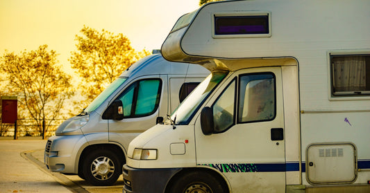 Two different camper vans with drawn curtains parked in a lot. A red sign and trees are in the background.