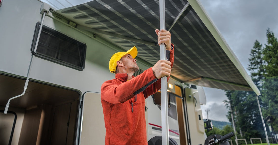 A man in a yellow baseball cap setting up an awning outside his RV as dark clouds roll over the campsite.
