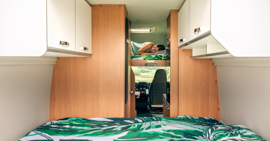 A woman sleeps alone on a bunk bed in a camper van. Green sheets cover the bed, and a sunroof is visible above her.