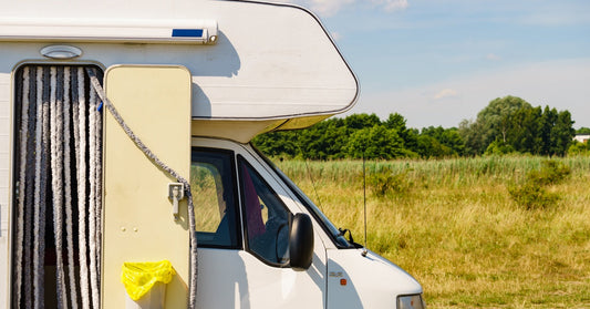 A camper van parked on a dirt road next to a grassy hill featuring a door curtain and a mounted trash can on its side.