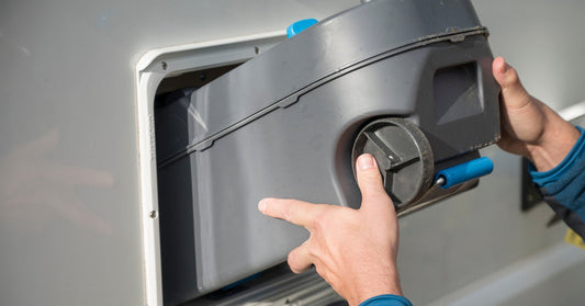 A parked camper van with an open side door sits behind public trash and recycling bins near the ocean on an overcast day.